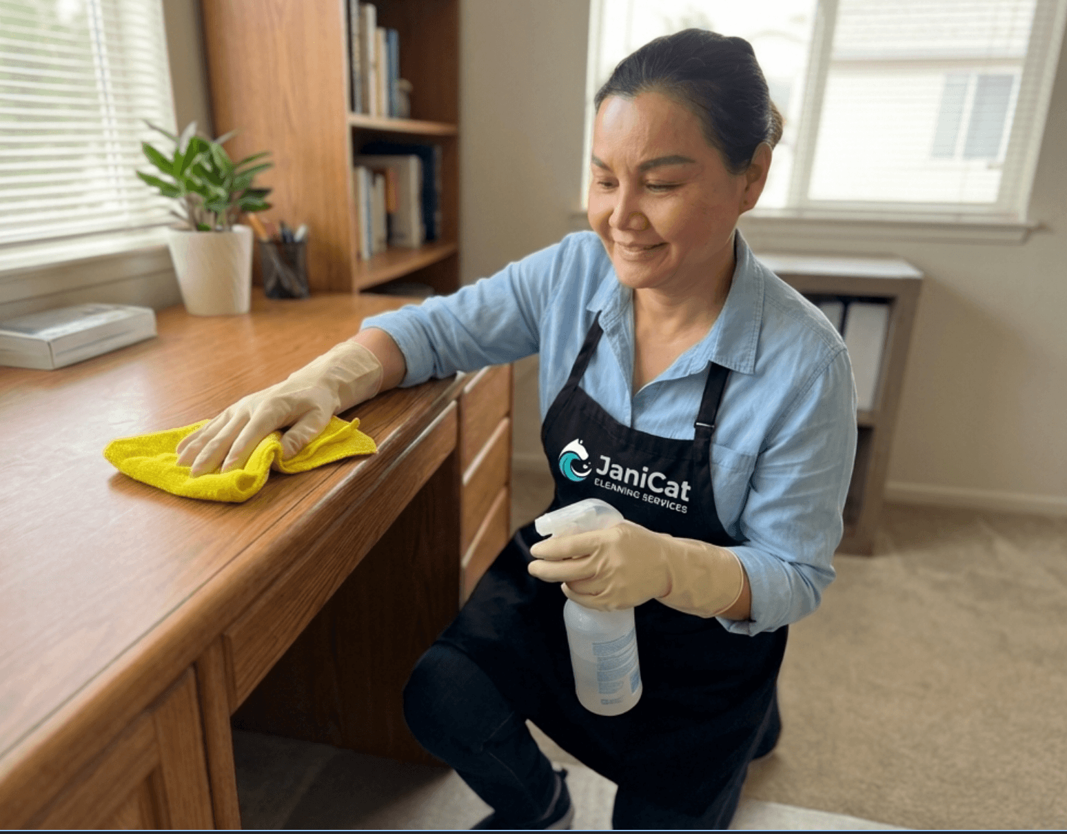 A smiling Janicat cleaner in her apron, wiping down a desk in a Seattle home office